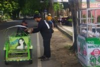 Anggota Komunitas Berbagi Sumenep (KBS) membagikan nasi bungkusan kepada pengendara dan pejalan kaki di simpang tiga Polres Sumenep, Jumat (26/12/2025).