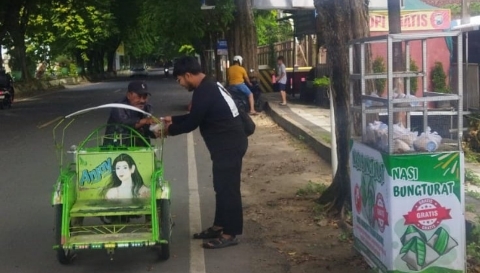 Anggota Komunitas Berbagi Sumenep (KBS) membagikan nasi bungkusan kepada pengendara dan pejalan kaki di simpang tiga Polres Sumenep, Jumat (26/12/2025).